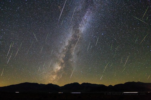 A starry night sky filled with the Milky Way and numerous shooting stars over a mountain landscape.