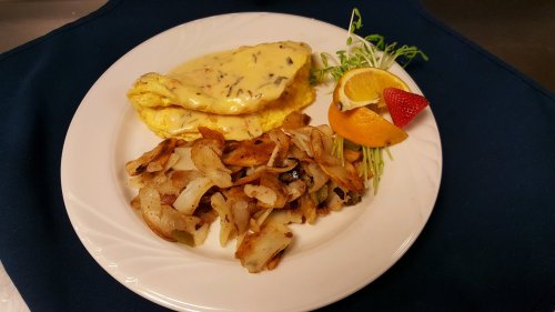 A plate featuring a cheese omelet, seasoned potatoes, and garnishes of orange and strawberry slices.
