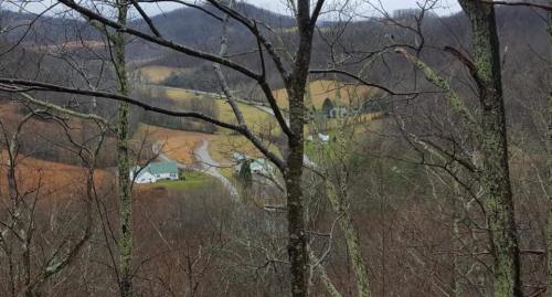 A scenic view of a rural landscape with houses nestled among trees and rolling hills, captured in a winter setting.
