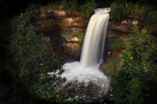 A serene waterfall cascading over rocky cliffs, surrounded by lush green foliage and a tranquil pool below.
