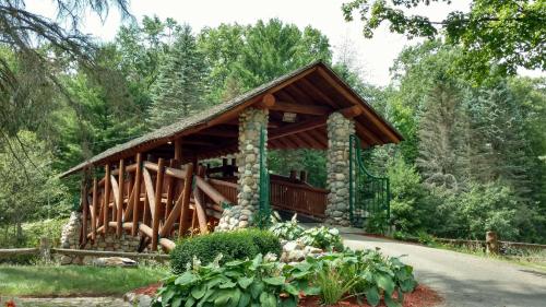 A rustic wooden pavilion with stone pillars, surrounded by lush greenery and a pathway leading to it.