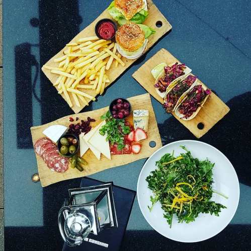 A spread of gourmet food including sliders, fries, tacos, cheese, olives, and a fresh salad on wooden boards.