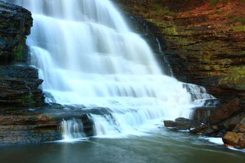 A serene waterfall cascading over rocky cliffs into a calm pool below, surrounded by lush greenery.