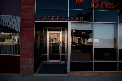 Exterior of a coffee bar with large glass windows and a sign reading "COFFEE BAR," showcasing a modern urban setting.