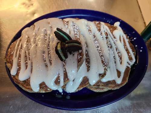 A plate of pancakes drizzled with white icing and topped with crushed cookies.