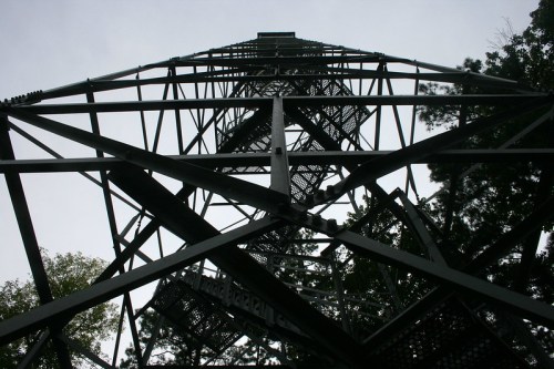 View looking up at a tall metal tower, showcasing its intricate lattice structure against a cloudy sky.