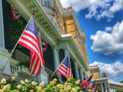 Historic building with American flags and lush greenery under a bright blue sky with fluffy clouds.