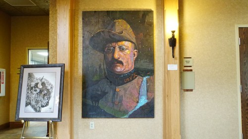 A large portrait of a man in military attire hangs on a wall, next to a framed artwork of a bison.