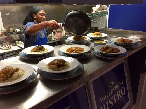 A chef plates dishes at The Waterfront Bistro, showcasing various meals on a counter.