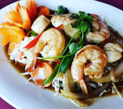 A vibrant plate of shrimp stir-fry with vegetables, garnished with carved carrots and fresh herbs.