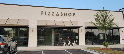 Exterior of a pizza shop with large windows, a sign reading "PIZZASHOP," and outdoor seating.