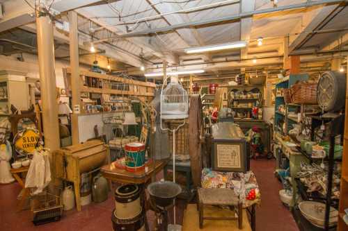 A cluttered antique shop filled with various vintage items, furniture, and decor in a warm, inviting atmosphere.