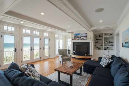 Bright coastal living room with large windows, ocean view, comfortable seating, and a cozy fireplace.