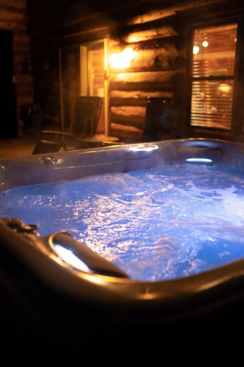 A bubbling hot tub with blue water, steam rising, set against a cozy log cabin backdrop.