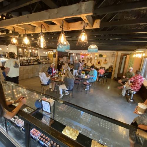 A cozy café interior with patrons seated at tables, warm lighting, and a display counter in the foreground.