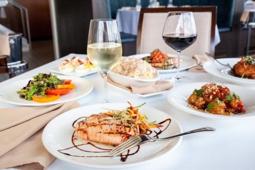 A beautifully arranged table with salmon, salads, rice, and two glasses of wine in an elegant dining setting.
