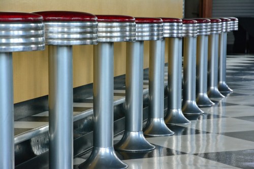 A row of retro diner stools with red seats and shiny metal bases, set against a black and white checkered floor.