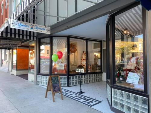 A storefront with large windows, a "Welcome" mat, and balloons outside, featuring holiday decorations and an "Open" sign.