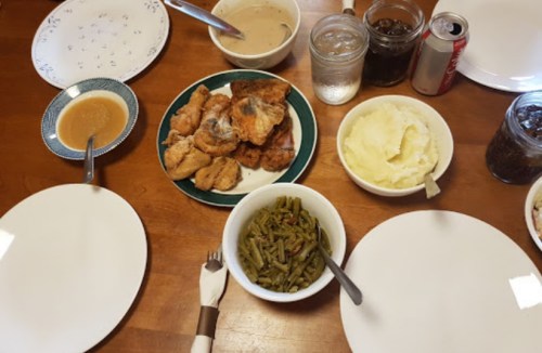 A dining table set with plates, fried chicken, mashed potatoes, green beans, gravy, and drinks.