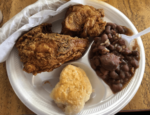 A plate of fried chicken, a biscuit, and a serving of red beans on a disposable white plate.
