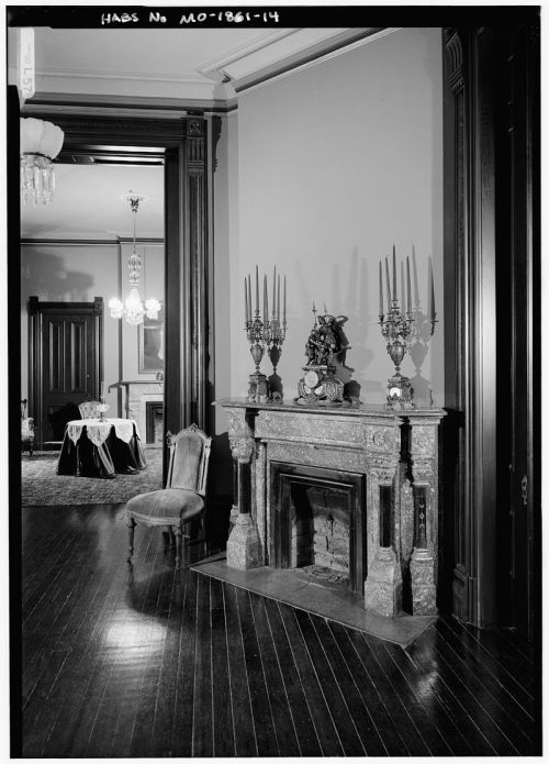 A vintage room featuring a marble fireplace with candelabras, a chair, and elegant decor in the background.