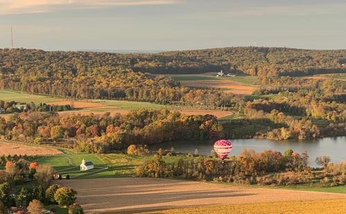 A colorful hot air balloon floats over a scenic landscape of fields, trees, and a calm lake during autumn.
