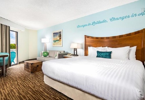 A cozy hotel room featuring a king bed, seating area, and balcony with a view, decorated in light colors.