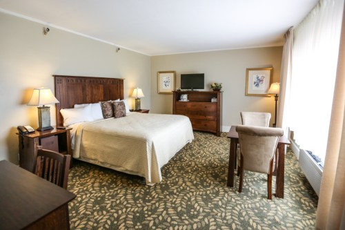 Cozy hotel room featuring a queen bed, desk, armchair, and warm lighting with a patterned carpet.