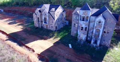 Aerial view of two abandoned, dilapidated houses surrounded by overgrown land and trees.