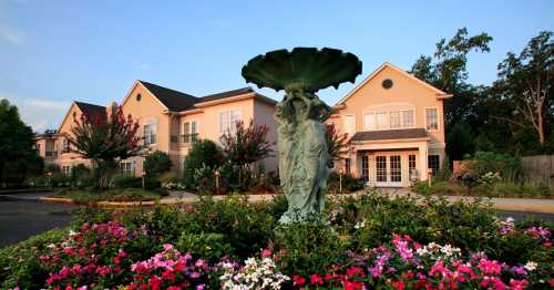 A decorative fountain surrounded by colorful flowers in front of a charming residential building at sunset.