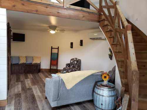 Cozy living space with a gray sofa, wooden stairs, and a barrel table, featuring warm lighting and simple decor.