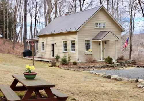 A charming yellow house with a porch, surrounded by trees and a picnic table in the foreground. An American flag is displayed.