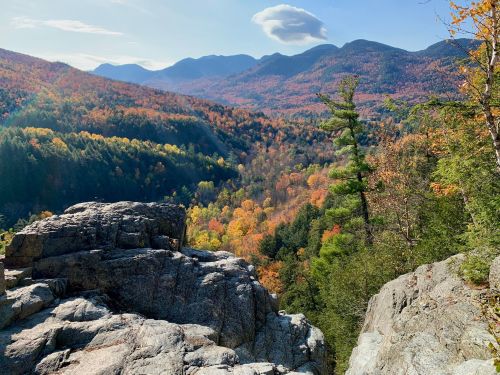 A scenic view of colorful autumn foliage in the mountains, with rocky outcrops in the foreground and a clear blue sky.
