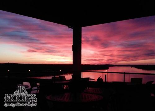 Silhouette of a balcony overlooking a river at sunset, with vibrant pink and purple skies.
