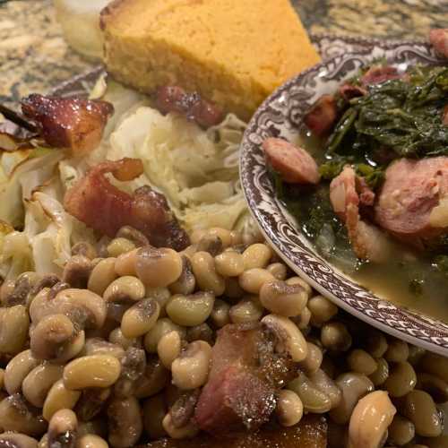 A plate of Southern comfort food featuring black-eyed peas, collard greens, cabbage, cornbread, and bacon.