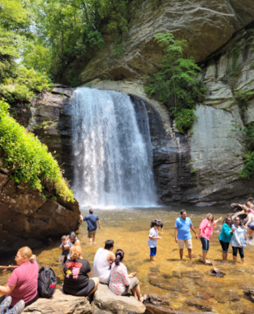 A waterfall cascades into a rocky pool, with people enjoying the water and surrounding nature.