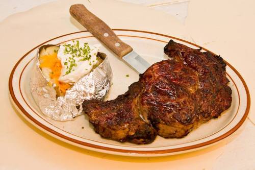 A juicy grilled steak served with a baked potato topped with cheese and sour cream on a plate.