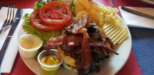 A hearty burger topped with bacon, mushrooms, and cheese, served with lettuce, tomato, and wavy potato chips.