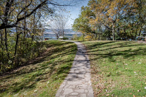 A winding stone path through a grassy area with trees and a view of a distant landscape under a clear sky.