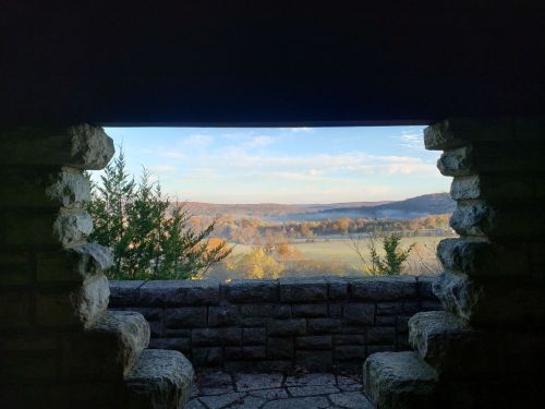 View from a stone structure overlooking a scenic landscape with trees and rolling hills in autumn colors.