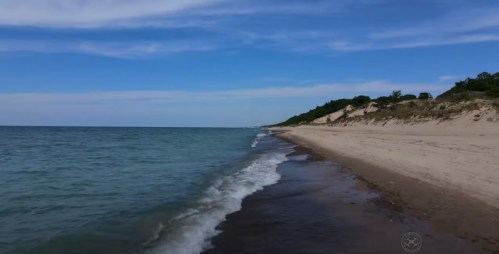 A serene beach scene with gentle waves lapping at the shore under a clear blue sky.