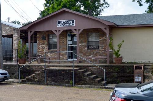 Exterior of Wesson Public Library, featuring a brick building with steps, a sign, and a book drop.