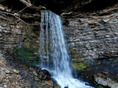 A serene waterfall cascading over rocky cliffs, surrounded by moss and natural stone formations.
