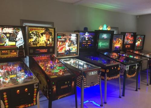 A row of colorful pinball machines with various themes and illuminated displays in a game room setting.