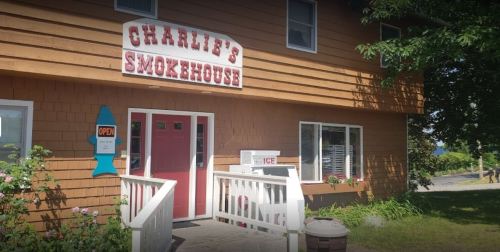 Exterior of Charlie's Smokehouse, featuring a wooden facade, open sign, and a white railing. Ice available outside.