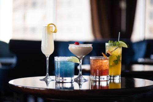 A variety of colorful cocktails on a wooden table, including a lemon drink, a margarita, and a mojito.