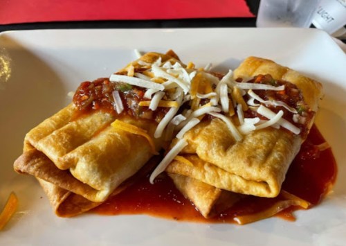 Two enchiladas topped with salsa and shredded cheese, served on a white plate.