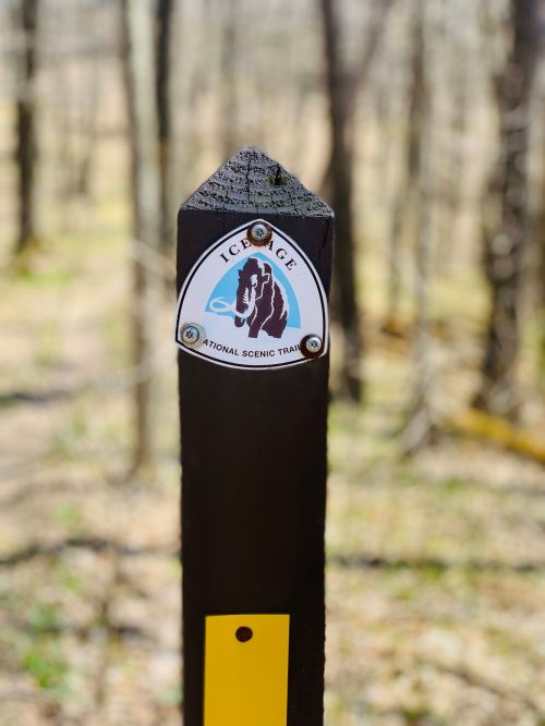 Signpost for the Ice Age National Scenic Trail, set in a wooded area with trees in the background.