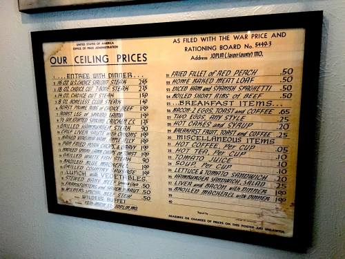 A vintage menu listing ceiling prices for various food items, framed and displayed on a wall.