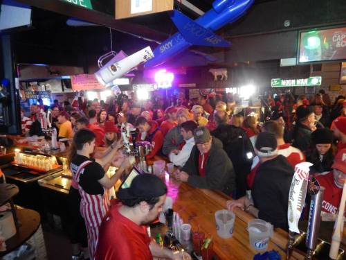 A lively bar scene filled with patrons in red and white attire, enjoying drinks and socializing.